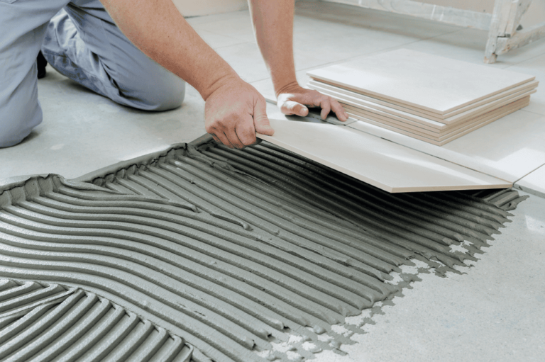 A person installing large floor tiles with adhesive mortar on a prepared surface.